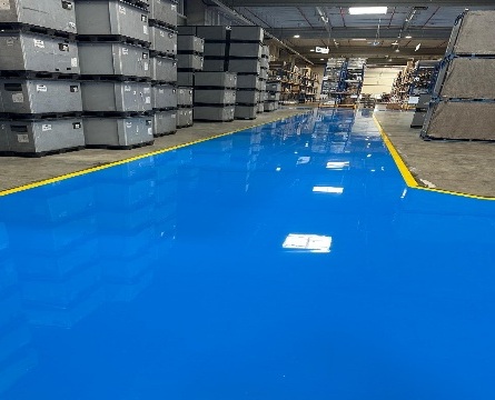 Lagerfläche mit glänzend blauem Epoxidharzboden und gelber Randmarkierung neben Gitterboxen